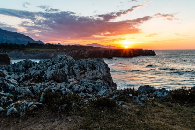 Fascinante vista del océano en calma y las rocas cerca de la orilla durante la puesta de sol