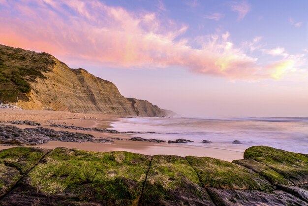 Fascinante vista de la playa rodeada de montañas rocosas durante la puesta de sol