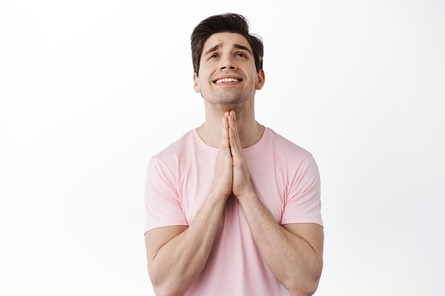 Foto gratuita por favor, dios me ayude. hombre joven desesperado rogando al señor, mirando hacia el cielo y suplicando, orando para que el deseo se haga realidad, necesita algo, de pie sobre fondo blanco.