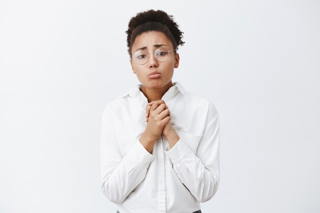 Por favor, te lo ruego. Afroamericano lúgubre y tímido con el pelo peinado, frunciendo los labios, frunciendo el ceño, tomados de la mano en oración sobre el pecho, pidiendo disculpas o ayuda