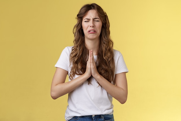 Por favor te lo suplico. Sollozando tímido inseguro angustiado linda chica llorona llorando molesto ojos cerrados haciendo muecas tomarse de las manos orar suplicando pidiendo un favor disculpándose sincera esperanza de piedad fondo amarillo