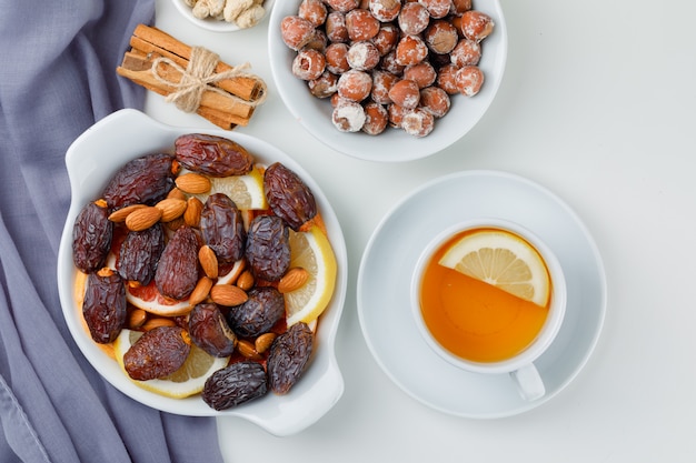 Fechas y almendras en plato con rodajas de cítricos, nueces, canela y té de limón vista superior en textil y mesa blanca