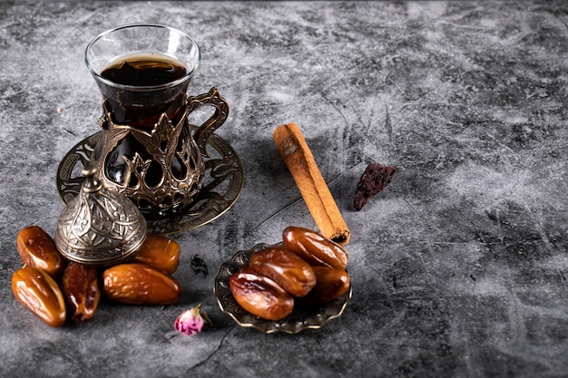 Fechas de delicias árabes en un mármol oscuro con un vaso de té y algunos palitos de canela