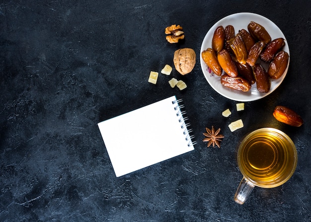 Foto gratuita fechas de frutas en plato con bloc de notas y té.