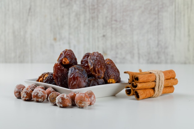 Fechas con palitos de canela y nueces en un plato, vista lateral.