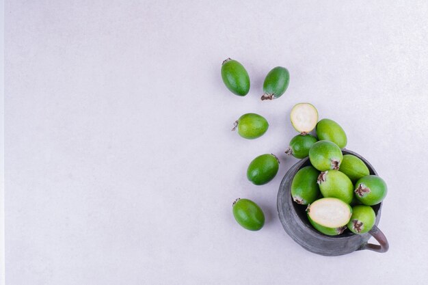 Feijoas verdes en maceta metálica sobre gris.