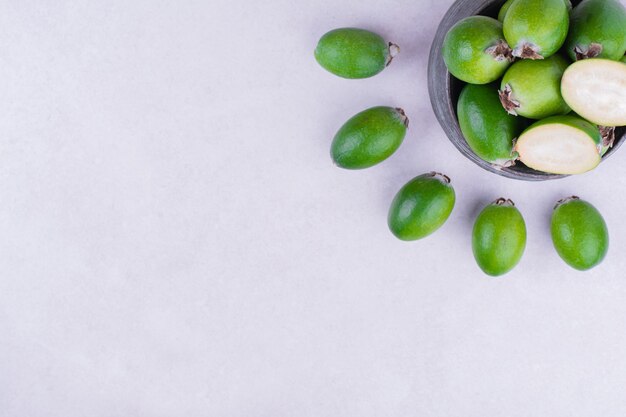 Feijoas verdes en maceta metálica sobre gris.