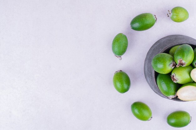 Feijoas verdes en una olla metálica sobre superficie blanca
