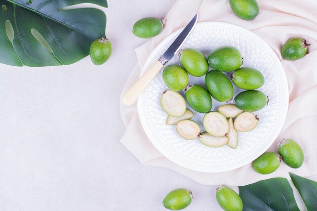 Feijoas verdes en un plato blanco con hojas alrededor