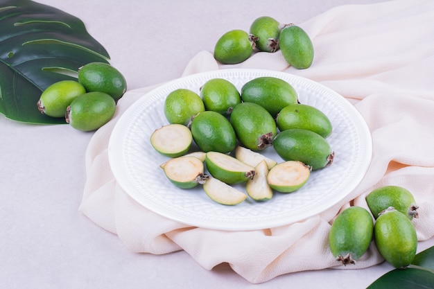 Feijoas verdes en un plato blanco con hojas alrededor