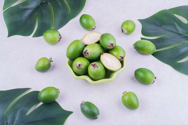 Feijoas verdes en una taza con hojas alrededor.