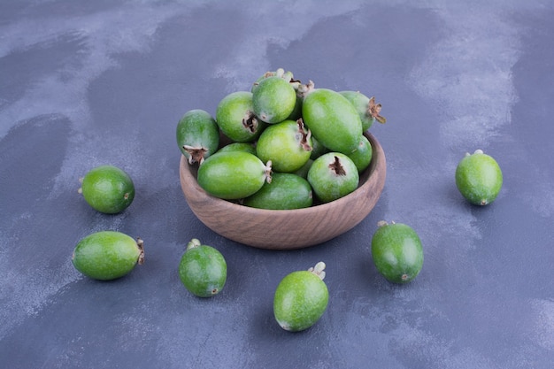 Feijoas verdes en una taza de madera sobre superficie azul