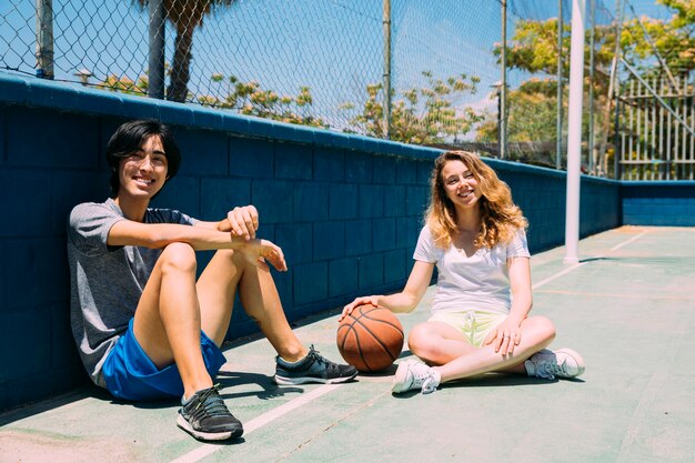 Felices adolescentes sentados en el campo de baloncesto