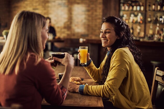 Felices amigas disfrutando mientras hablan en un pub