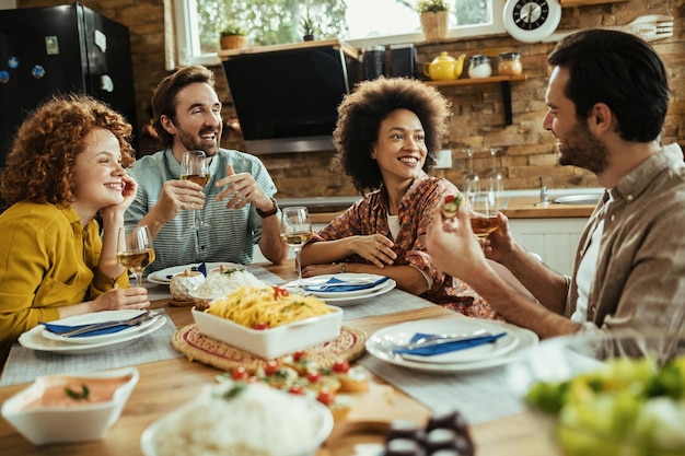 Felices amigos comunicándose mientras almuerzan y beben vino en el comedor. El foco está en la mujer afroamericana.