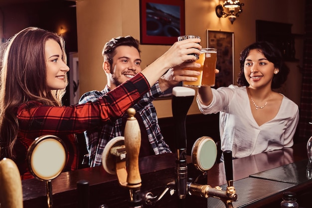 Felices amigos multirraciales haciendo un brindis con cerveza en el bar o pub.