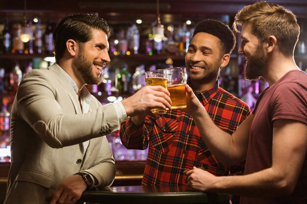 Felices amigos varones sonrientes tintinean con jarras de cerveza