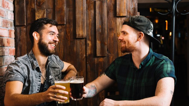 Felices amigos varones tostado vaso de bebidas alcohólicas