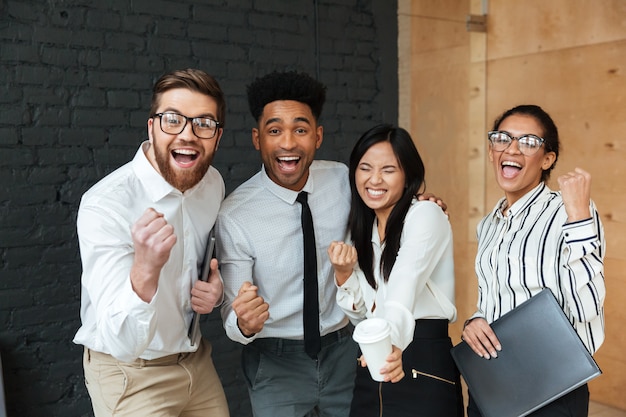 Felices colegas de negocios jóvenes emocionados hacen gesto ganador.