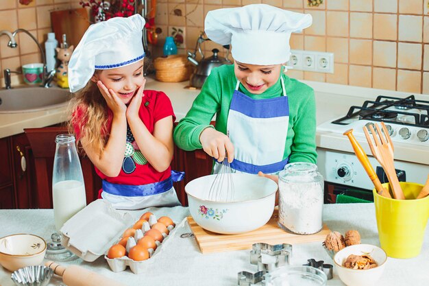 Los felices dos niños divertidos preparan la masa, hornean galletas en la cocina