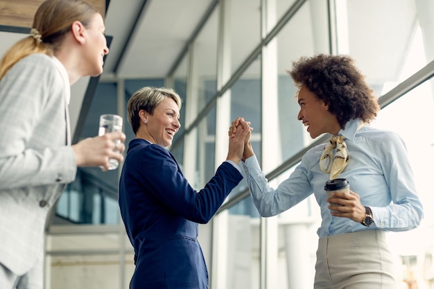 Felices empresarias tomados de la mano mientras saludan en un pasillo