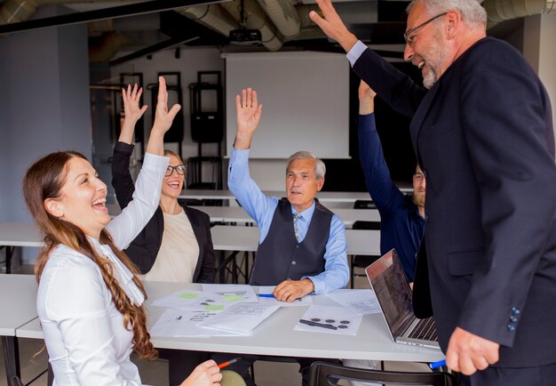 Felices empresarios exitosos levantando sus manos en la reunión del consejo