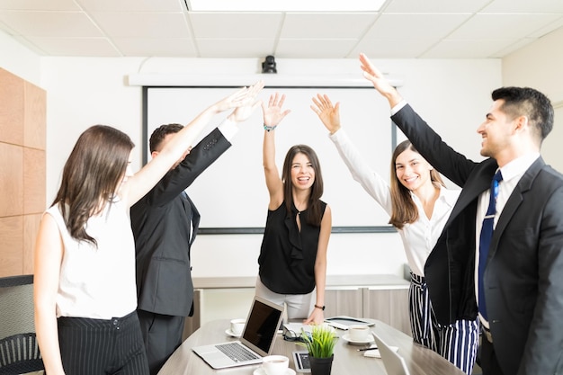 Felices empresarios multiétnicos y empresarias levantando la mano para celebrar en la sala de juntas