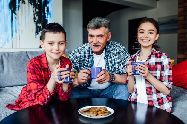 Felices generaciones. Anciano sonriente alegre bebiendo té mientras disfruta del tiempo con sus nietos.