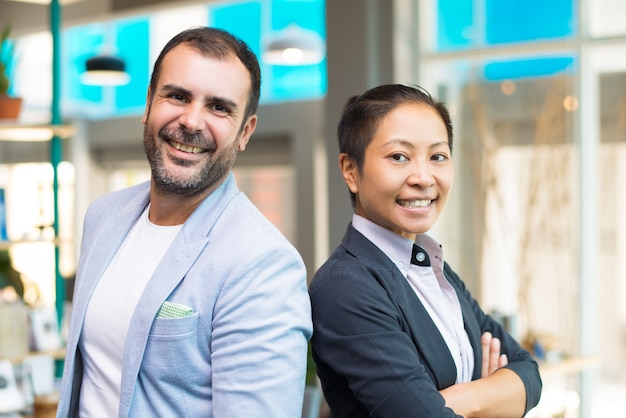 Felices gerentes asiáticos y latinos sonrientes y parados uno al lado del otro