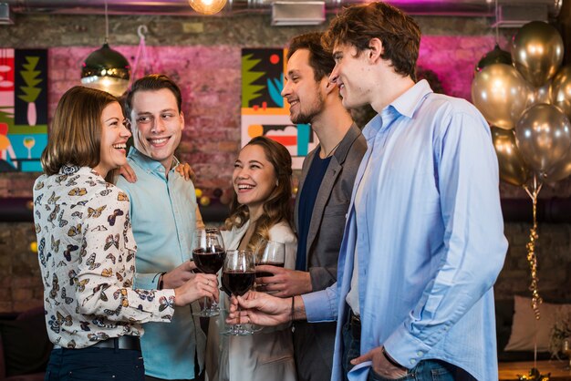 Felices jóvenes amigos celebrando y brindando vino en el bar