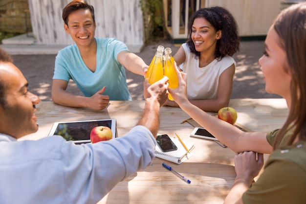 Felices jóvenes amigos multiétnicos estudiantes afuera bebiendo jugo