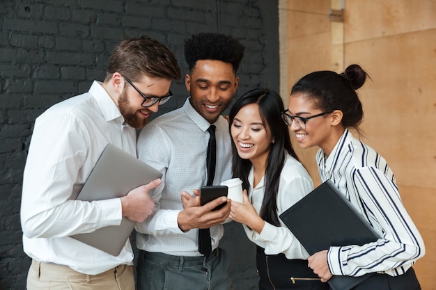 Felices jóvenes colegas de negocios mediante teléfono móvil.