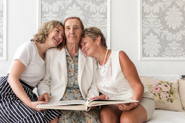 Felices mujeres de tres generaciones sentadas en un sofá con un álbum de fotos.