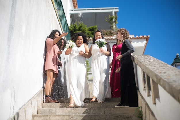 Felices novias e invitados a la boda. Dos mujeres con vestidos blancos bajando las escaleras. Invitadas arrojándoles arroz