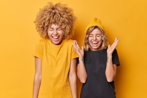 Felices y optimistas jóvenes compañeras se ríen a carcajadas de una broma graciosa y se sienten eufóricas expresando emociones positivas vestidas casualmente aisladas sobre un fondo amarillo vívido Concepto de personas y felicidad