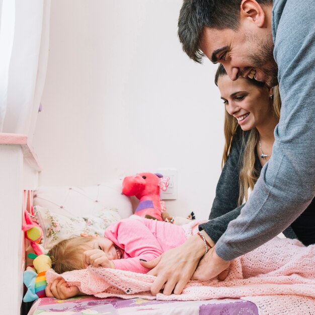 Felices padres caminando a su hija en la cama