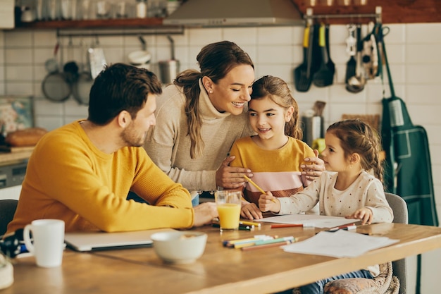 Felices padres disfrutando con sus pequeñas hijas que están coloreando el papel en casa