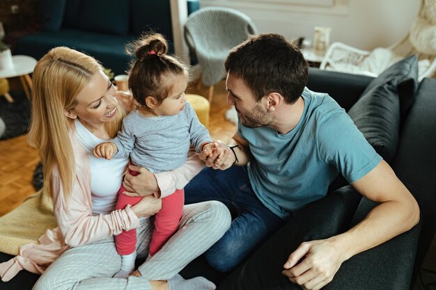 Felices padres divirtiéndose con su pequeña hija mientras hablan con ella en casa.