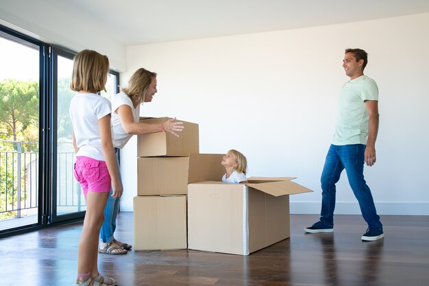Felices padres y dos hijas divirtiéndose mientras desempacan cosas en su nuevo piso vacío