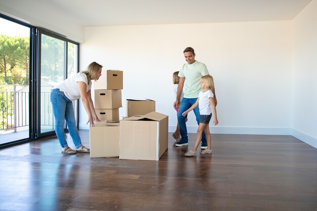 Felices padres e hijas abriendo cajas y desempacando cosas en su nuevo piso vacío