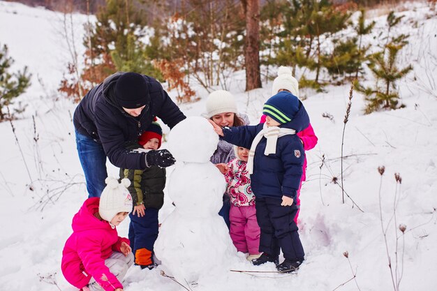 Felices padres e hijos crean un gran muñeco de nieve.