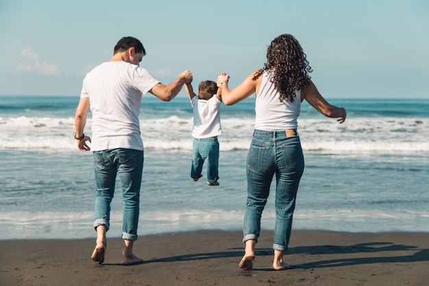 Felices padres lanzando a su bebé en playa soleada