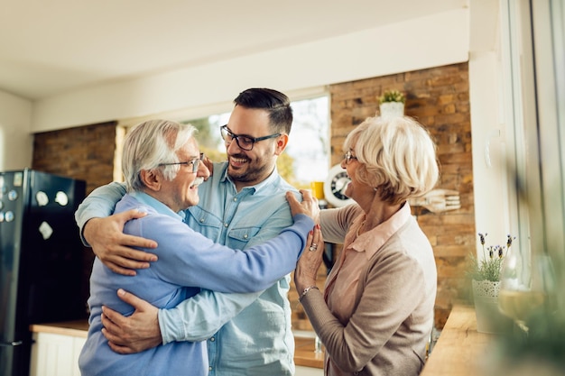 Felices padres mayores y su hijo adulto divirtiéndose mientras saludan en la cocina