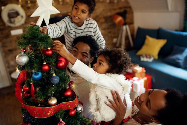 Felices padres negros ayudando a sus hijos a decorar el árbol de Navidad en casa
