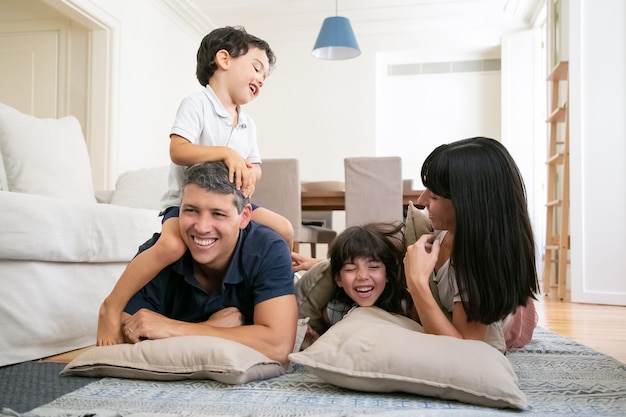 Felices padres riendo y dos niños pequeños disfrutando de tiempo de diversión en casa