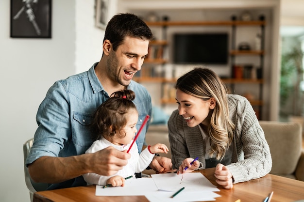 Felices padres y su pequeña hija divirtiéndose mientras colorean en el papel