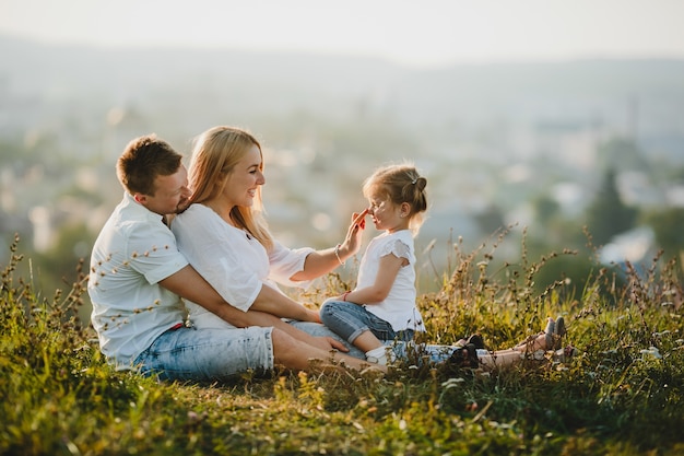 Los felices padres y su pequeña niña descansan en el césped en un hermoso día de verano