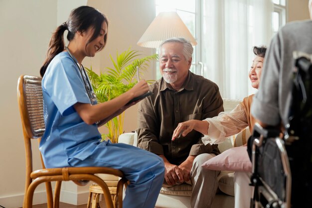 Felicidad Alegre anciana y hombres hablando con una enfermera cuidadora médica que tiene una consulta de control de salud en la sala de estarCuidadores con una pareja mayor sentada en la sala de estar en un hogar de ancianos