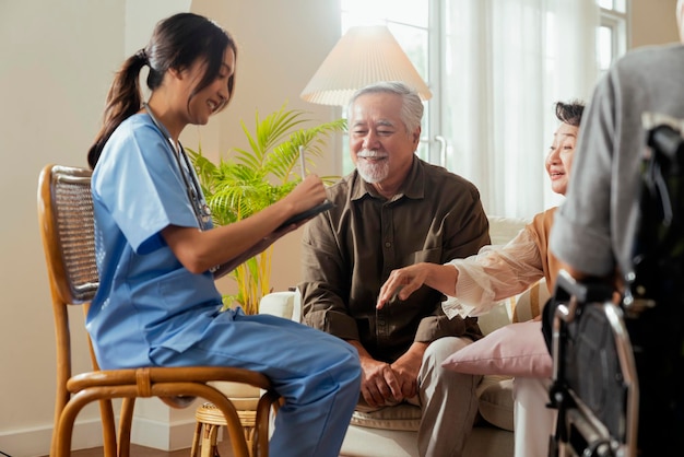 Felicidad Alegre anciana y hombres hablando con una enfermera cuidadora médica que tiene una consulta de control de salud en la sala de estarCuidadores con una pareja mayor sentada en la sala de estar en un hogar de ancianos