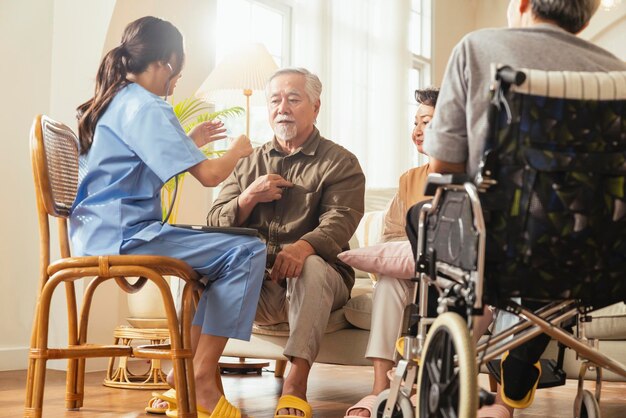 Felicidad Alegre anciana y hombres hablando con una enfermera cuidadora médica que tiene una consulta de control de salud en la sala de estarCuidadores con una pareja mayor sentada en la sala de estar en un hogar de ancianos